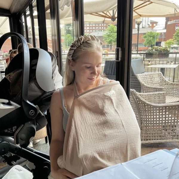 Woman sitting at a table with a baby in a sling in an outdoor cafe setting